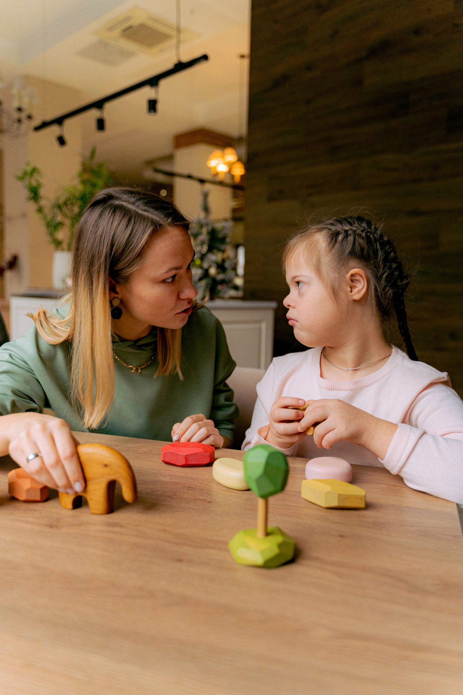 A therapist and a young girl playing with wooden shapes at a table