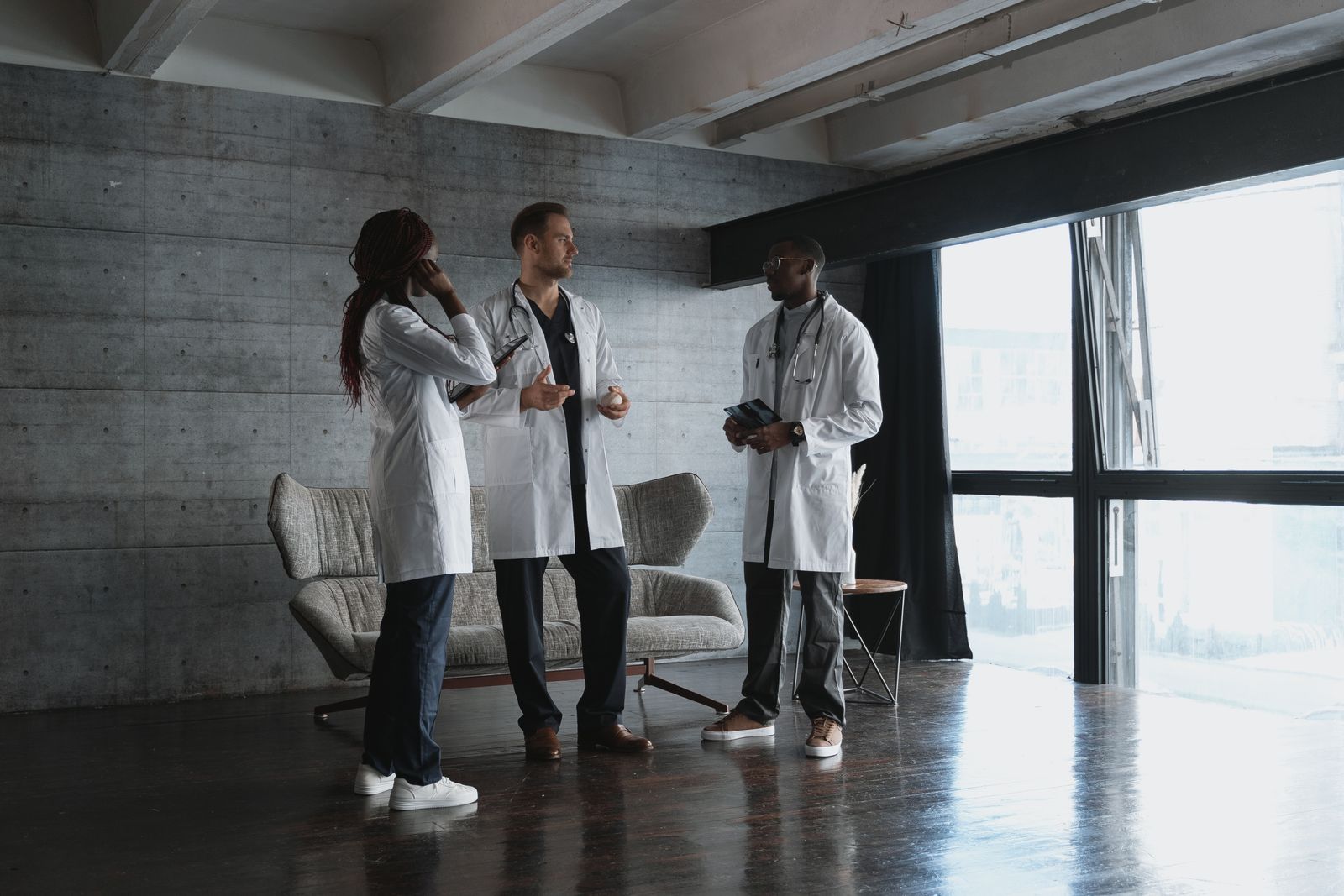 Three clinicians in white coats talking in a bright meeting room