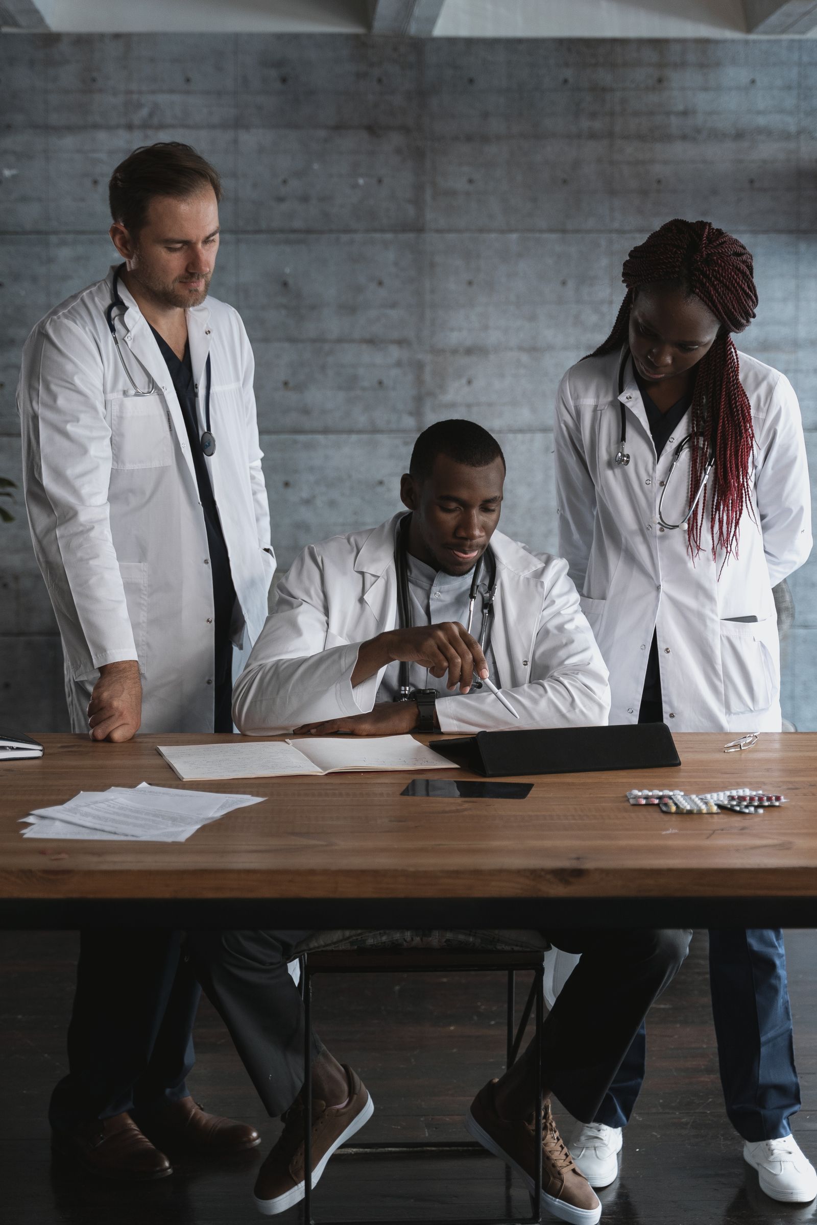 Three clinicians in white coats look over documents at a table