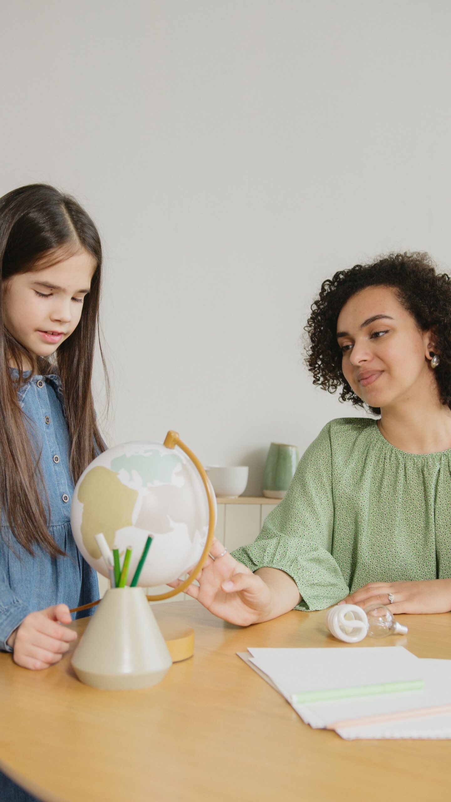 A teacher and a girl working together at a table with a small globe